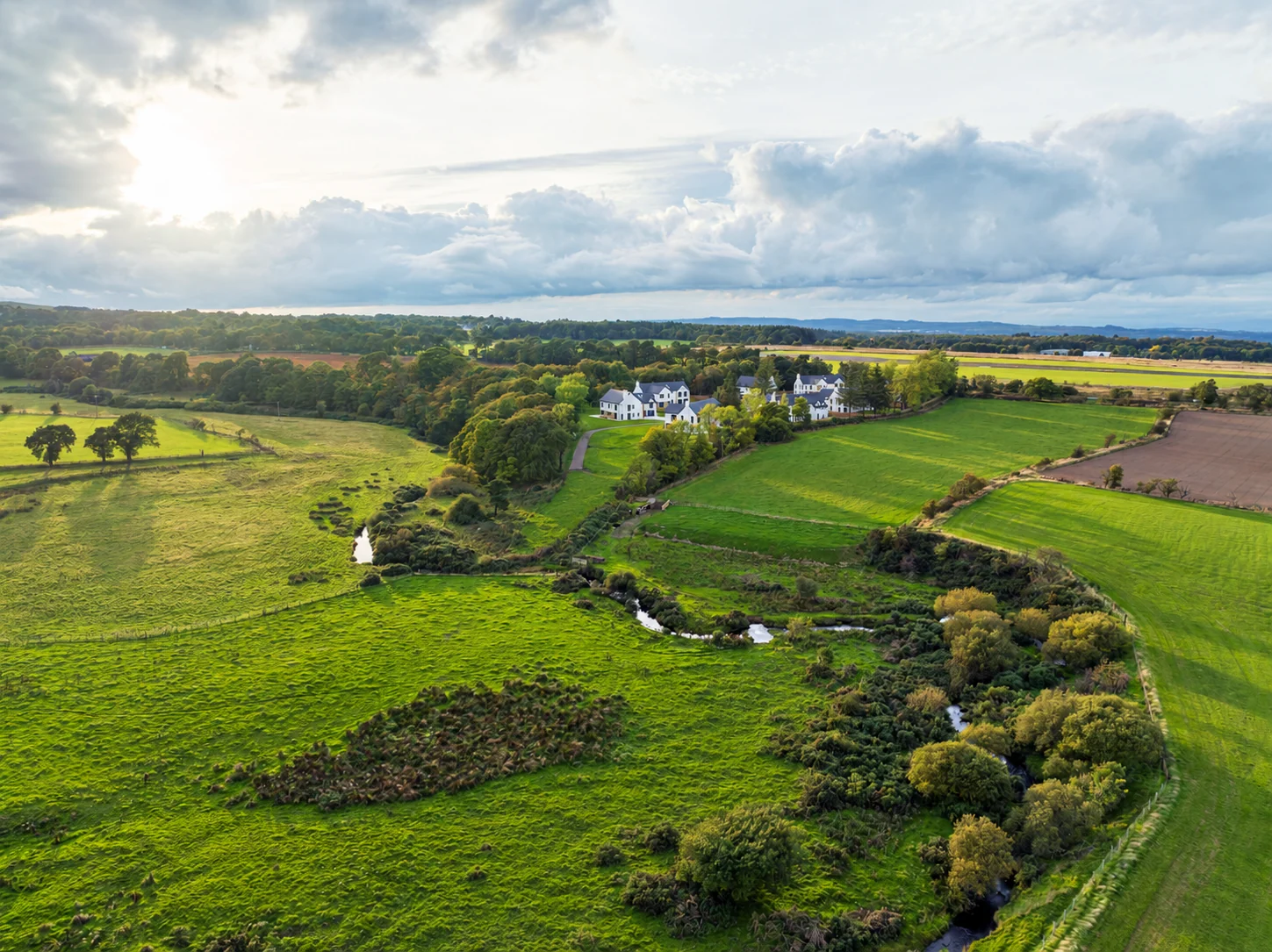 The homes set beside woodland and a river within the surrounding countryside